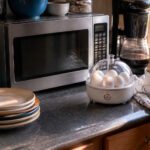 Cluttered kitchen countertop with a microwave and egg cooker in morning light.